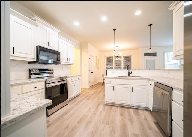 kitchen featuring appliances with stainless steel finishes, a sink, white cabinets, a peninsula, and a chandelier