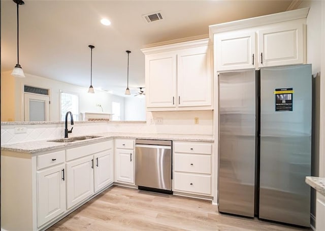 kitchen featuring stainless steel appliances, a sink, a peninsula, white cabinetry, and light stone countertops