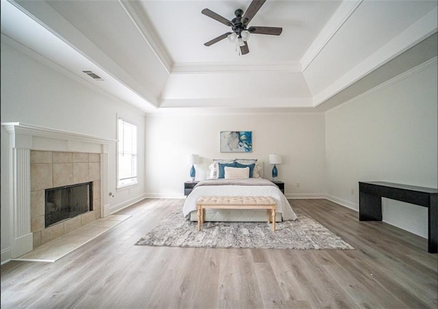 bedroom featuring a tray ceiling, wood finished floors, ornamental molding, baseboards, and a tile fireplace