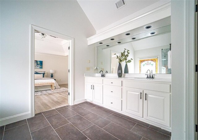 ensuite bathroom featuring double vanity, baseboards, tile patterned flooring, and vaulted ceiling