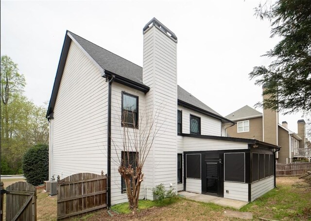 back of house featuring a gate, a chimney, a sunroom, fence, and central air condition unit
