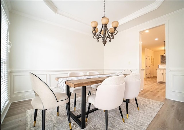 dining room with light wood-style floors, a chandelier, ornamental molding, a wainscoted wall, and a decorative wall