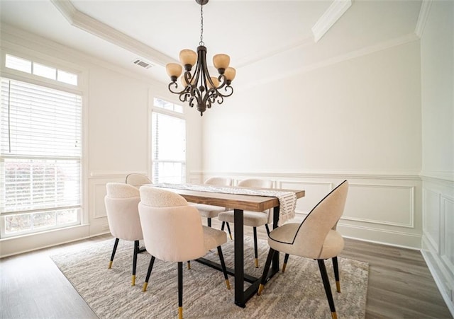 dining area featuring a chandelier, ornamental molding, dark wood-type flooring, a decorative wall, and a raised ceiling