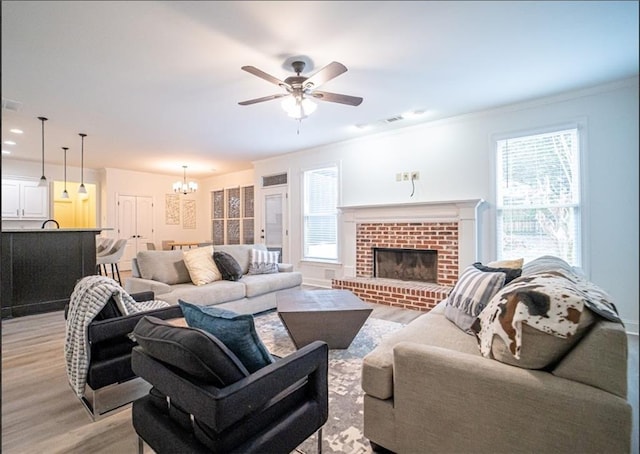 living area featuring light wood finished floors, a chandelier, ceiling fan, plenty of natural light, and crown molding