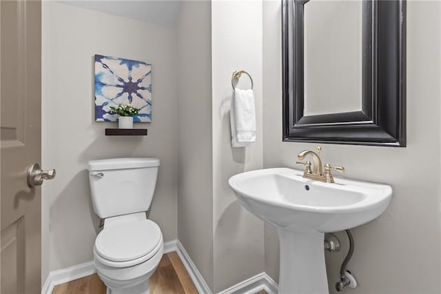 half bathroom with toilet, wood finished floors, and baseboards