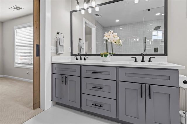 full bathroom with a tile shower, baseboards, and double vanity
