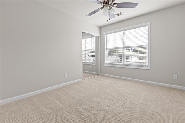 spare room featuring light colored carpet, ceiling fan, and baseboards