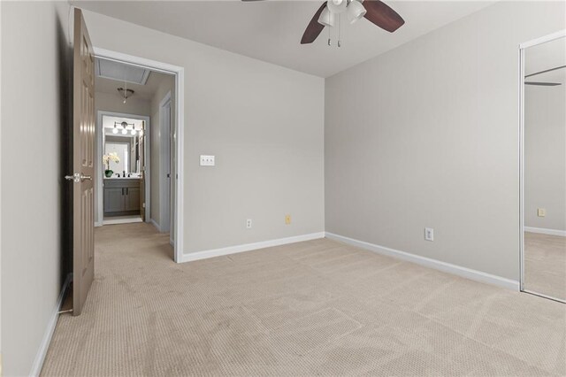 unfurnished bedroom featuring attic access, light colored carpet, baseboards, and ceiling fan