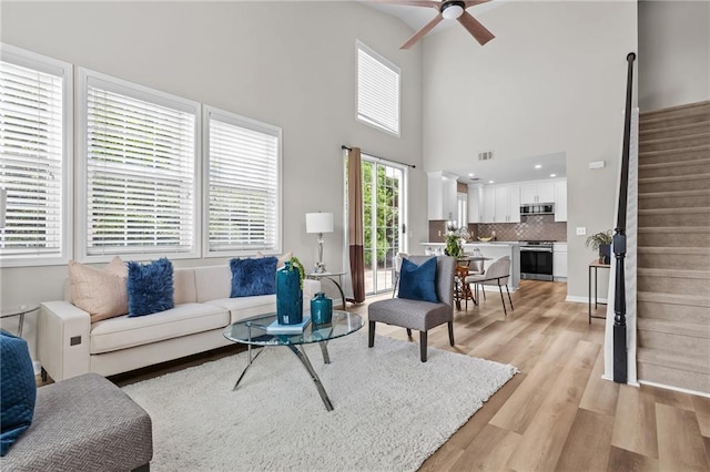 living room featuring stairs, ceiling fan, light wood-style floors, and a towering ceiling