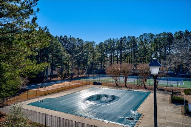view of swimming pool with fence and view of wooded area