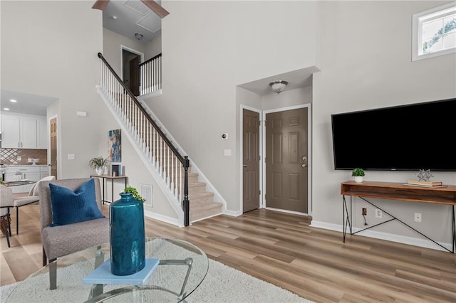 foyer entrance with a high ceiling, stairs, light wood-style floors, and baseboards