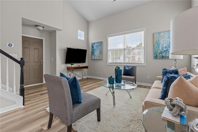 living room with light wood-style flooring, stairway, baseboards, and high vaulted ceiling