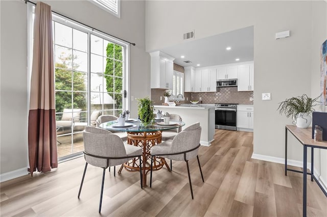 dining area with light wood-style floors, a towering ceiling, baseboards, and recessed lighting