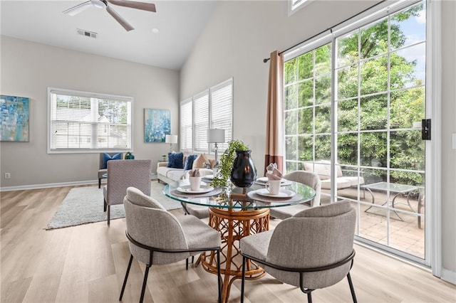 dining area with a ceiling fan, light wood-type flooring, high vaulted ceiling, and baseboards