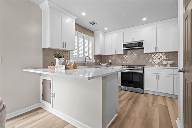 kitchen featuring stainless steel appliances, light wood finished floors, white cabinetry, light countertops, and a peninsula