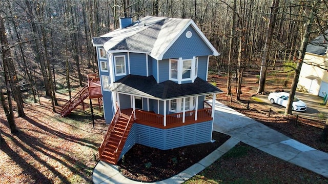 view of front of property with a porch, stairs, a wooded view, a shingled roof, and a chimney