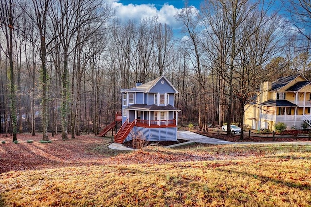 back of house with stairs, a wooded view, covered porch, and a chimney