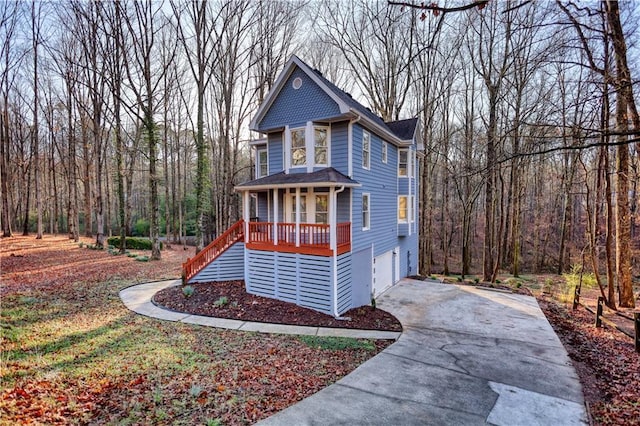 view of front facade featuring an attached garage, stairway, covered porch, a view of trees, and driveway