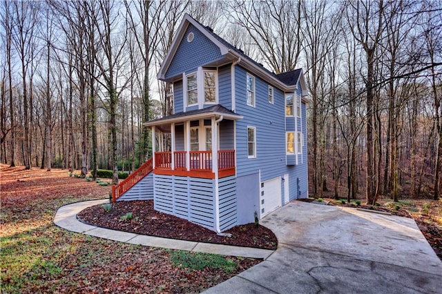 view of front facade with a wooded view, stairway, covered porch, driveway, and an attached garage