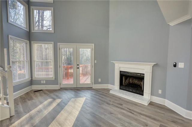 unfurnished living room with a fireplace with raised hearth, baseboards, french doors, a high ceiling, and wood finished floors