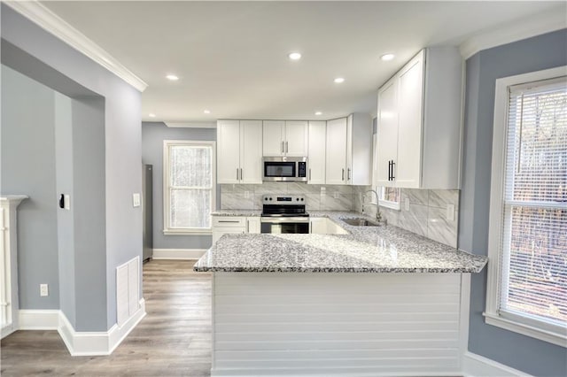 kitchen featuring light stone countertops, a peninsula, a sink, stainless steel appliances, and backsplash