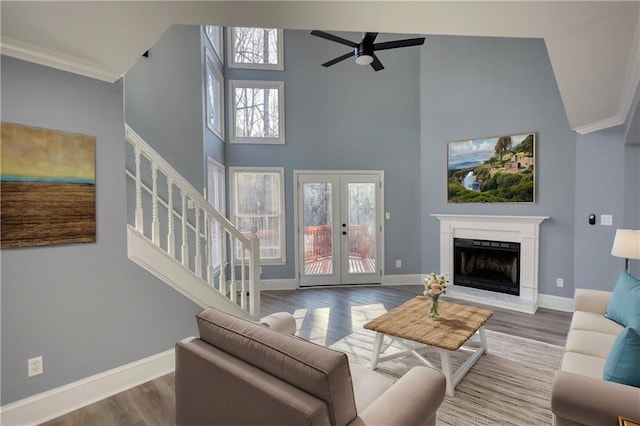 living area featuring a fireplace with raised hearth, a high ceiling, baseboards, and wood finished floors