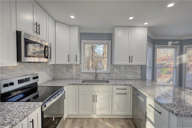 kitchen featuring a sink, stainless steel appliances, a peninsula, white cabinets, and crown molding