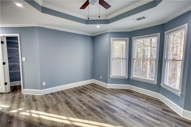 empty room with visible vents, crown molding, a raised ceiling, and wood finished floors