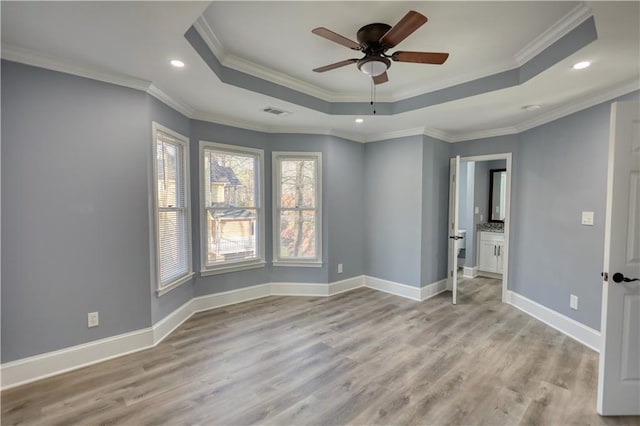 spare room featuring a tray ceiling, baseboards, and light wood finished floors