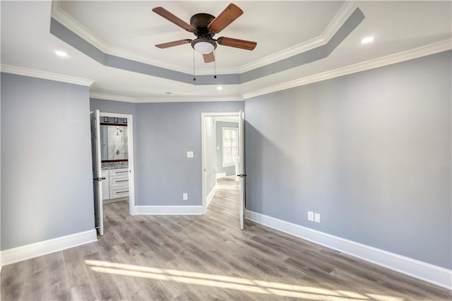 empty room with ornamental molding, baseboards, a tray ceiling, and wood finished floors