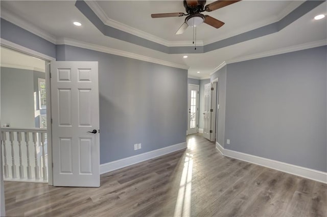 empty room featuring a raised ceiling, wood finished floors, baseboards, and ornamental molding