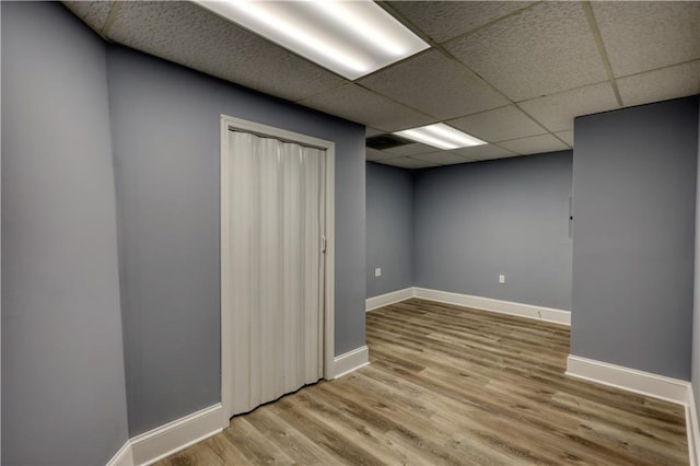 finished below grade area featuring a paneled ceiling, baseboards, and wood finished floors