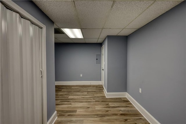 corridor with a drop ceiling, baseboards, and wood finished floors