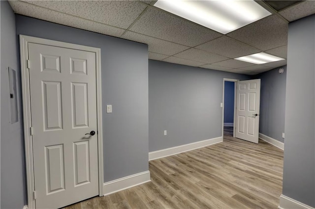 empty room featuring a drop ceiling, baseboards, and wood finished floors