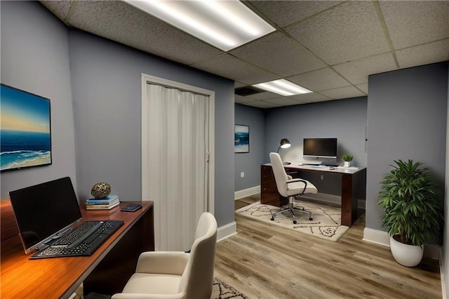 office space with baseboards, a paneled ceiling, and light wood-style floors