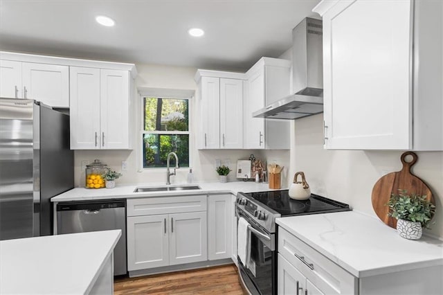 kitchen featuring stainless steel appliances, a sink, white cabinets, light countertops, and wall chimney range hood