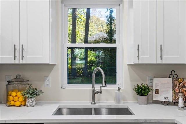 kitchen featuring white cabinetry, light stone counters, and a sink