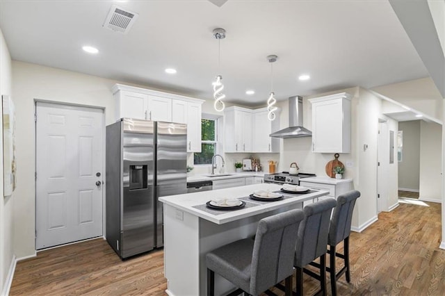 kitchen with stainless steel appliances, visible vents, white cabinets, a sink, and wall chimney range hood