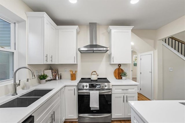 kitchen featuring electric range, wall chimney range hood, a sink, and white cabinetry