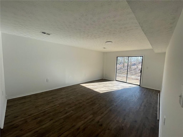 spare room with dark wood-style flooring, a textured ceiling, visible vents, and baseboards