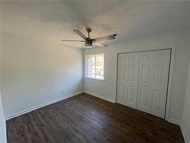 unfurnished bedroom with a textured ceiling, visible vents, dark wood-style floors, and baseboards