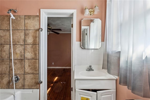 bathroom with ceiling fan, vanity, tiled shower / bath combo, and tile walls