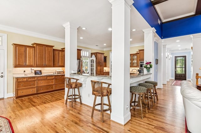 317 Red Gate Overlook, Canton, GA 30115 - kitchen with brown cabinetry, ornate columns, crown molding, a breakfast bar, and light wood-style flooring