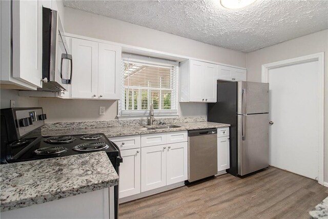 kitchen with white cabinetry, light hardwood / wood-style floors, appliances with stainless steel finishes, and a textured ceiling