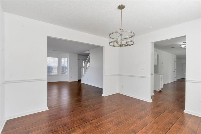 unfurnished room with an inviting chandelier, dark hardwood / wood-style flooring, and a textured ceiling