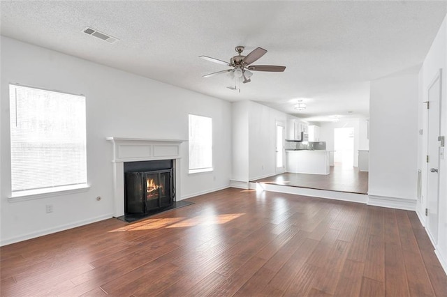 unfurnished living room featuring dark wood-type flooring, ceiling fan, and a textured ceiling