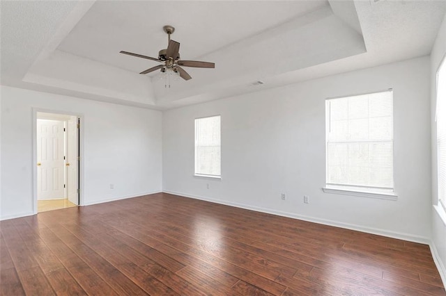 empty room with a raised ceiling, ceiling fan, and dark hardwood / wood-style flooring