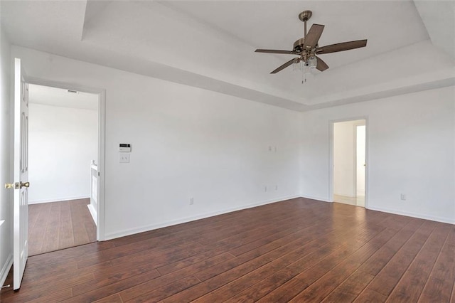 empty room with ceiling fan, dark hardwood / wood-style flooring, and a tray ceiling