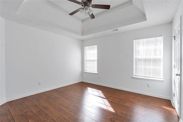 spare room with a raised ceiling, ceiling fan, and dark hardwood / wood-style flooring