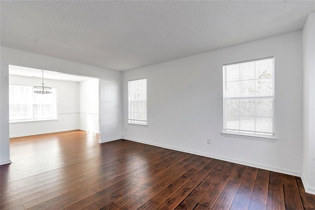 spare room featuring dark wood-type flooring and an inviting chandelier